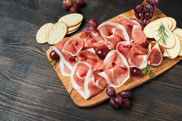 Traditional Italian antipasti prosciutto crudo with grapes and crackers on a wooden plate. Spanish jamon. Food for aperitif and dinner lunch in the restaurant 