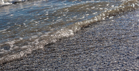 Natural marine texture. Sea wave runs onto the shore of small stones. View from above and at an angle. Blue sea and wet pebbles. Texture and background.