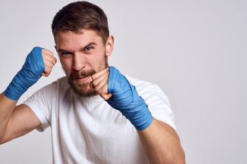 A sportive man in a white T-shirt boxing bandages on his hands practicing blow exercises improving skills