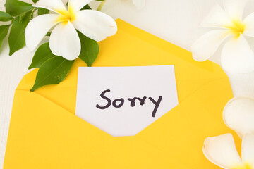 sorry message card in yellow envelope with white flowers fragnipani arrangement flat lay postcard...