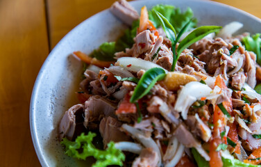 Spicy tuna salad and Decor with Tea leaf on White plate on wooden table. Homemade thai style, Selective focus.