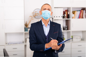 Portrait of positive business man in protective mask with folder of documents at office