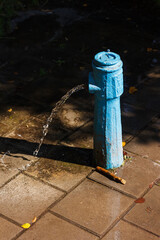Broken old drinking column in the park. Strong stream of water from the pump column