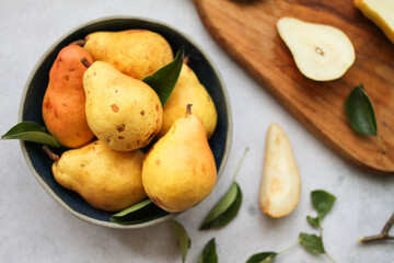 A bowl of fresh pears and a wooden cutting board with pear slices. Top view.