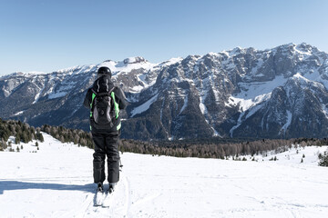 A man stands on the side of a mountain against the backdrop of the snow-capped Dolomites. Concept for sports, landscape, people.