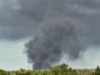 A Burning plastic recycling place causes a big pile of dark, black thick smoke on a sky blue summer day. Danger, sorrow. Terrorist attack or explosion.