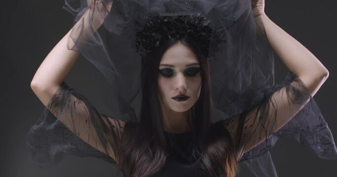 Mystical girl in black veil looking at the camera and smiles, the celebration of Halloween, portrait of a beautiful gothic woman.