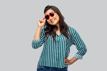 love, summer and valentines day concept - happy asian young woman in heart shaped sunglasses over grey background