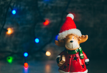 deer dressed as santa claus on the background of a dark wall with a christmas garland