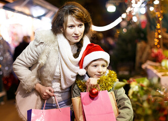 Fototapeta na wymiar Smiling preteen boy having fun on Xmas outdoor fair with mother, selecting decoration for home