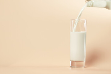 Soy milk in the glass by pouring from bottle as pastel orange colors background. Healthy food and vegetarian concept.