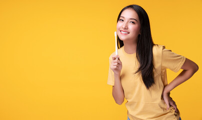 Smile young woman holding white toothbrush in her hand while looking at camera over isolated yellow background with copy space. Good oral and dental health concept.