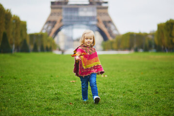 Fototapeta premium Adorable toddler girl near the Eiffel tower on a fall day in Paris, France