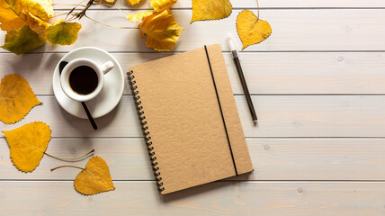 Workspace with notebook, pen, autumn leaves, and coffee cup.