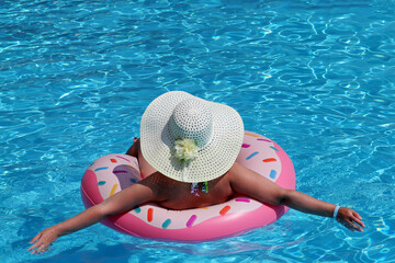 Woman in hat and bikini swimming on inflatable donut ring in the pool. Beach vacation, relax and leisure concept