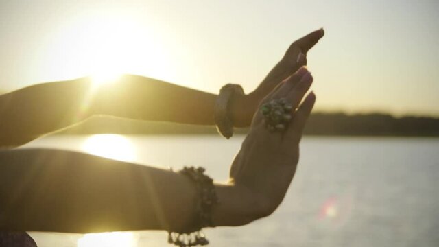 Plastic female dancing hands with bracelets on the background of the sunset over the lake. Dance with hands close up in nature