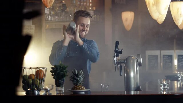 Barkeeper in apron mixing fruit cocktail in smoky bar shot in 4k