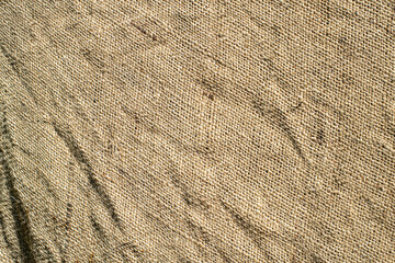 Fototapeta na wymiar The texture of an old burlap rag. Shot in the bright sun, visible creases and damage to the cotton fabric.