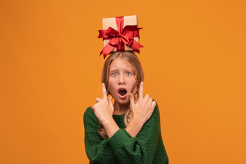 Charming blonde teen hold gift box on her head. Studio shot, yellow background. New Year Birthday Holiday concept