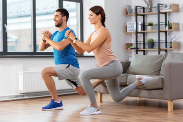 Obraz premium sport, fitness, lifestyle and people concept - smiling man and woman exercising and doing lunge using sofa at home