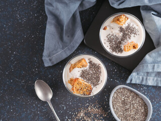 No baked cheesecake dessert with crushed carrots biscuits and chia seeds in glass jar on dark background. Ideas and recipes for healthy breakfast. Copy space for text. Top view or flat-lay.