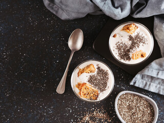 No baked cheesecake dessert with crushed carrots biscuits and chia seeds in glass jar on dark background. Ideas and recipes for healthy breakfast. Copy space for text. Top view or flat-lay.
