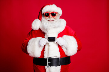 Portrait of his he nice handsome cheerful cheery rich wealthy bearded Santa holding in hand plastic card shop cash pay wireless secure payment isolated bright vivid shine vibrant red color background