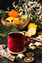 Obraz na płótnie Canvas hot tea in a red mug in a new year's atmosphere. Christmas morning. A mug with a drink next to Christmas tree branches, oranges, spices and cookies