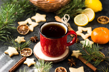 Obraz na płótnie Canvas hot tea in a red mug in a new year's atmosphere. Christmas morning. A mug with a drink next to Christmas tree branches, oranges, spices and cookies