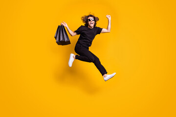 Fototapeta na wymiar Bought everything I wanted. Full length body size portrait of man jumping high with packages on black friday wearing black outfit isolated on bright yellow color background
