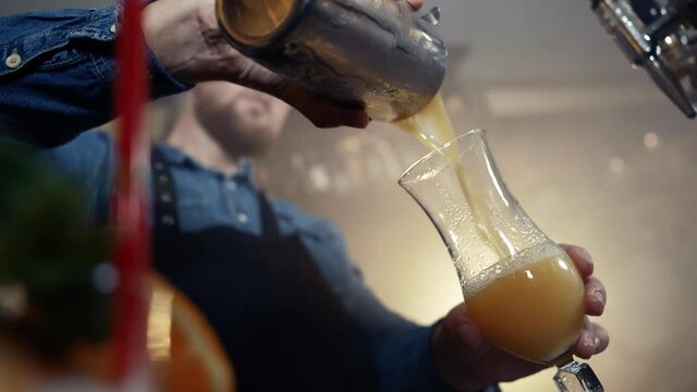 Barkeeper wearing apron spilling cocktail in glass in smoky bar shot in 4k super slow motion