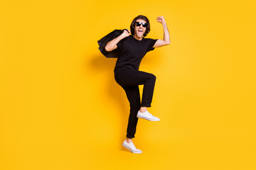 Fototapeta na wymiar Full length photo of young man hold shopping packages open mouth wear black t-shirt pants white sneakers sunglass isolated yellow color background