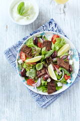 Tasty Salad with Grilled Beef Pieces, Cherry Tomatoes, feta Cheese and Kalamata Olives. Bright wooden background. Top view. 
