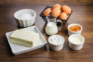 Ingredients for making cheesecake. Fresh chicken eggs, sugar, milk, flour, cream, cheese, jam. On a wood table top background.