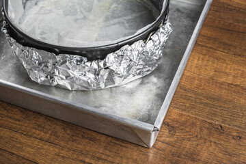 A cake tin line with wax paper and wrap in aluminum foil on a tray for putting a water bath before...