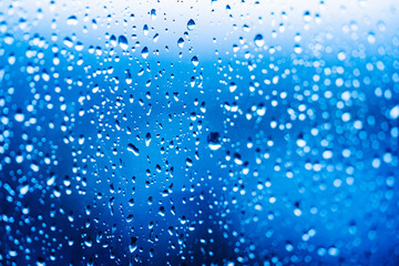 Naklejka na ściany i meble Droplets of water on enlighted glass background. Rain water drops running down. Water droplets falling on glass surface.