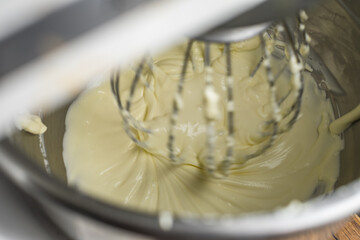 Close up creaming cream cheese to soften in the food mixer machine bowl for making cheesecake or other bakery products.