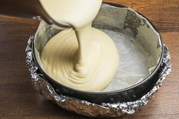 Pouring cake mixture into a cake tin line with paper and wrap with aluminum foil for baking cheesecake.