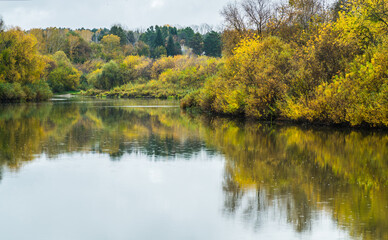 Calm river with trees on the shores in rainy autumn day. Autumn landscape. 