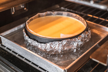 Baking cheescake in cake tin line with paper and wrap with aluminum foil in water bath in oven.