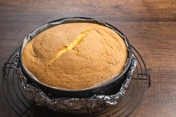 Fototapeta na wymiar Freshly baked fluffy japanese cheesecake in cake tin on a cooling rack on wood table top.