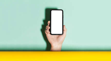 Close-up of male hand holding smartphone with mockup between two backgrounds of yellow and aqua menthe color.