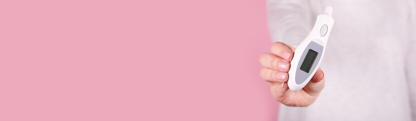 Electronic thermometer in hands on a pink background. Close up photo, copy space template, banner.