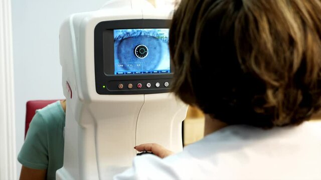 Optician doctor working with the refractometer machine. Eye exam for young woman at optical store.