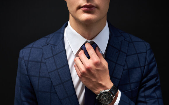 cropped business man straighten a tie isolated over black background. young guy in formal suit preparing for meeting