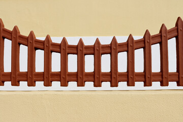 Brown decorative fence against the background of a yellow and white wall