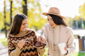 two young and cheerful woman enjoying delicious cakes in city park in a positive and energetic mood