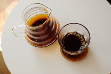 Black filter coffee served in a jug and a glass on a white round table. Top view. Specialty third wave concept