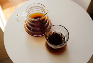 Black filter coffee served in a jug and a glass on a white round table. Top view. Specialty third wave concept