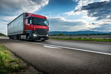 Red semi trailer lorry truck passing on a highway driving at beautiful dramatic sunset....
